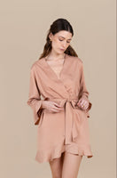 Woman wearing a blush and tan robe against a beige background