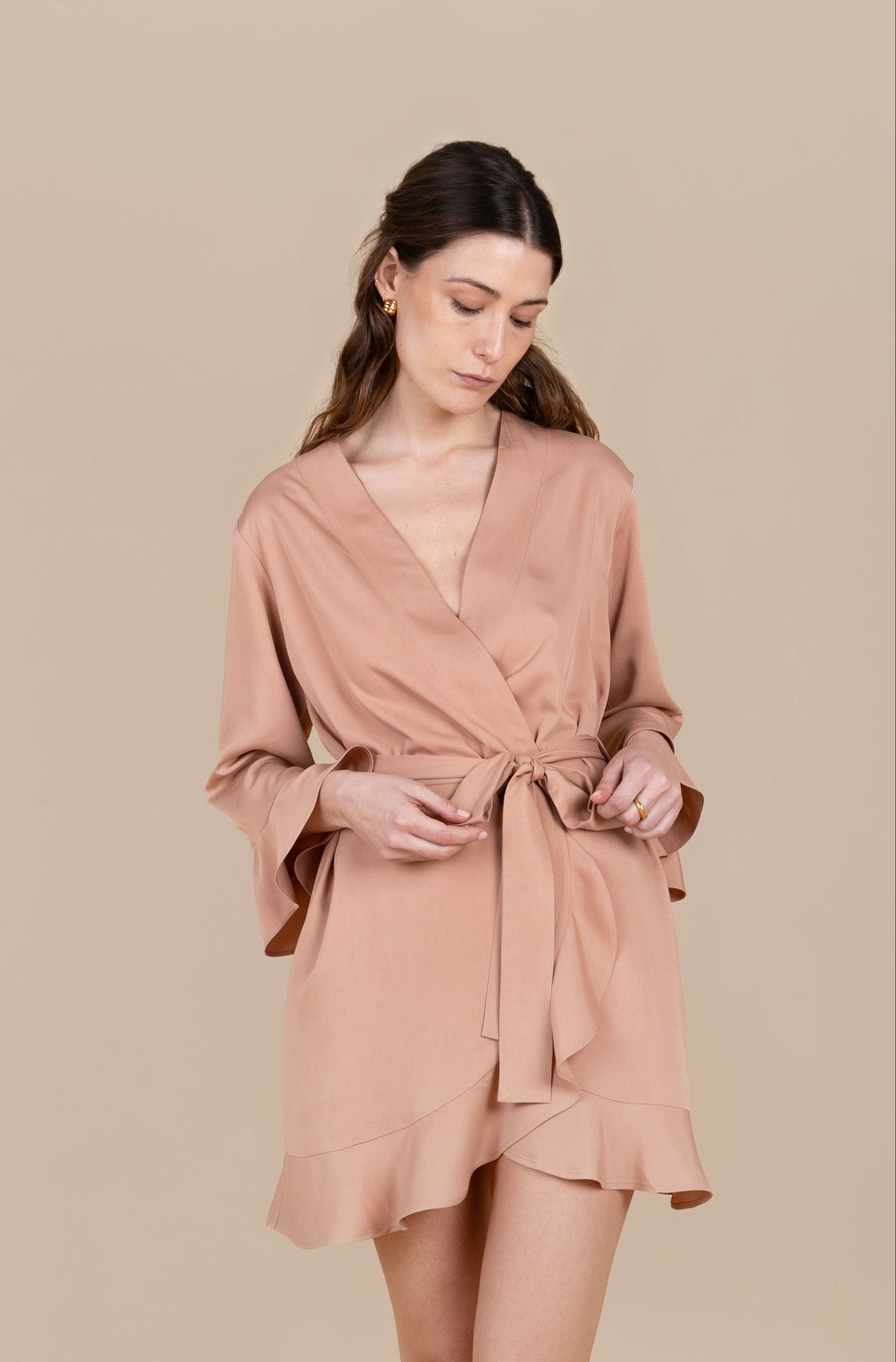 Woman wearing a blush and tan robe against a beige background